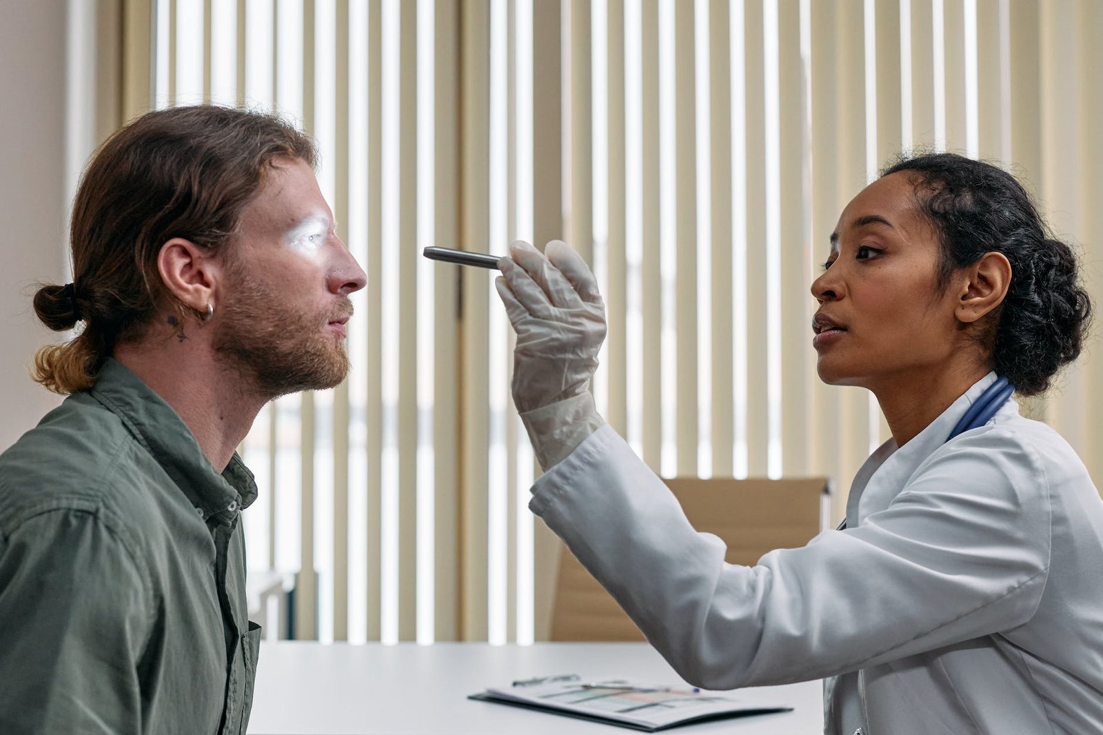 woman in white suit looking at mans eye with pen flashlight