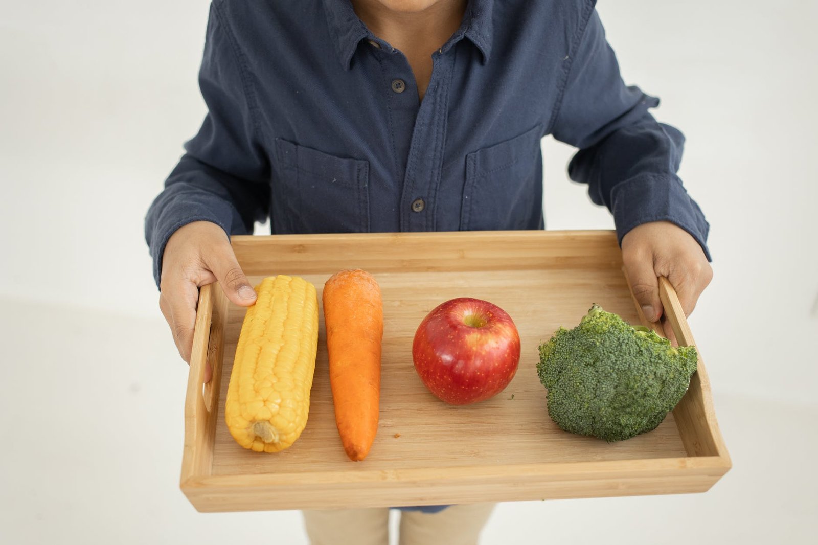 crop child standing in studio with tray with assorted fresh vegetables and fruits