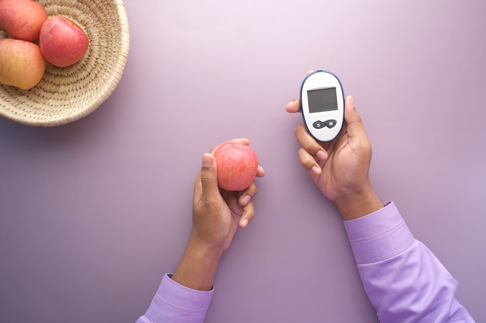 hands holding an apple and a glucometer
