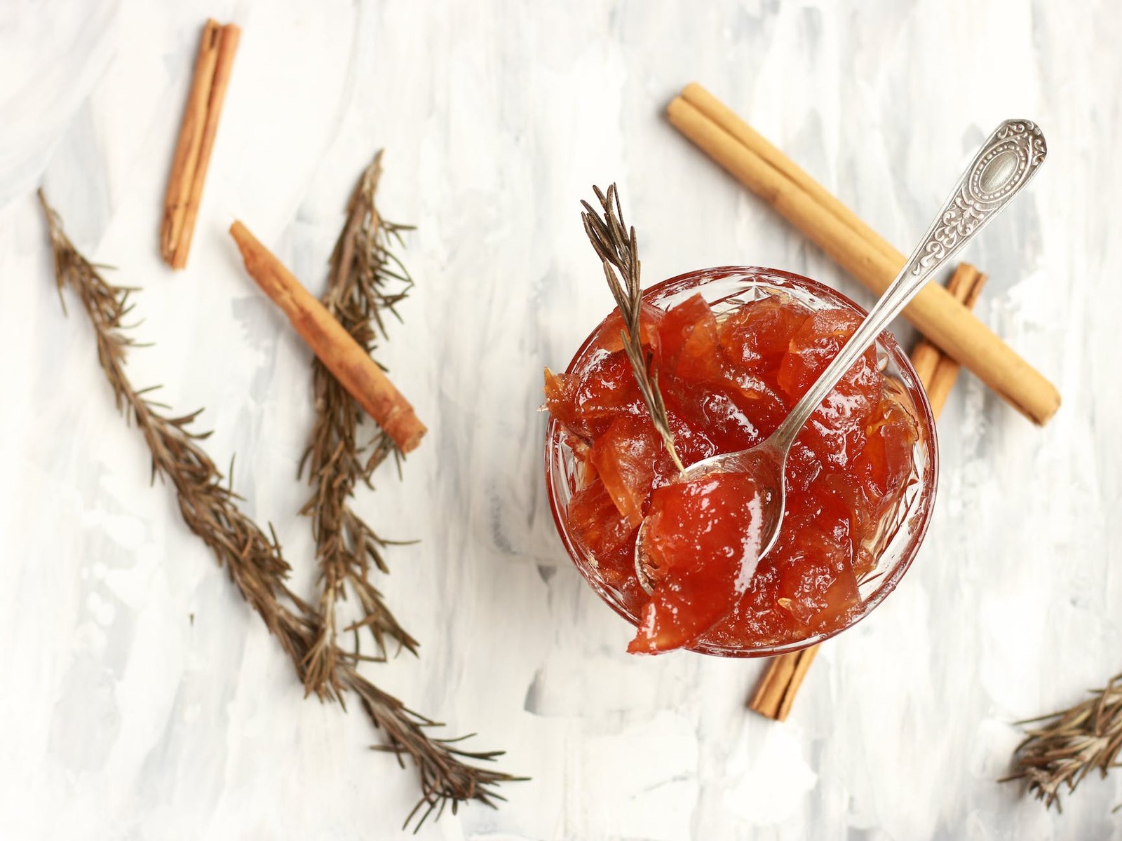 glass bowl of jam with rosemary sprigs and cinnamon sticks