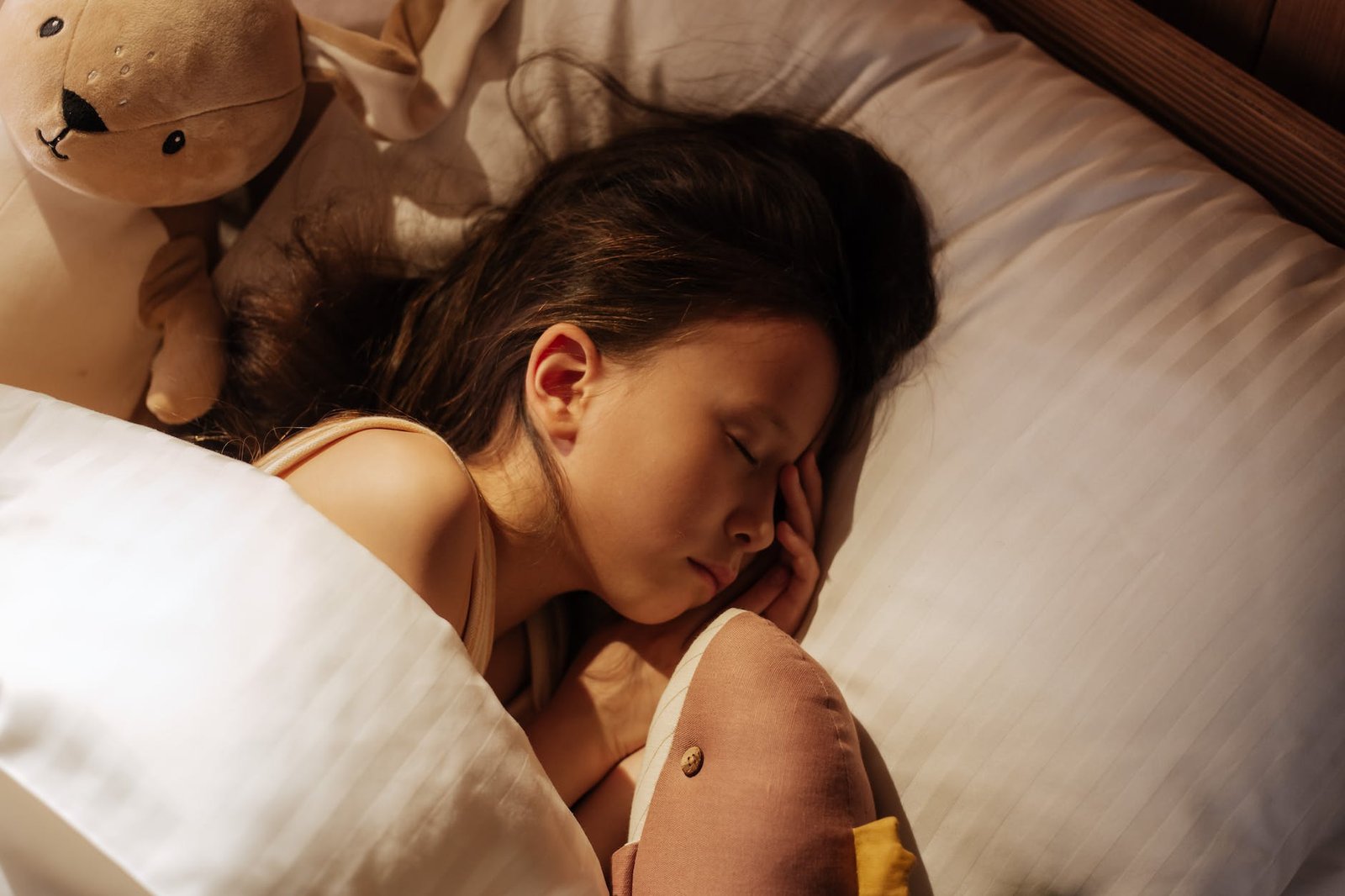 girl sleeping in bed between cuddling toys